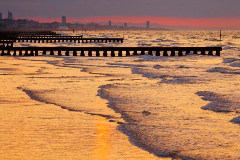 Alba sulla spiaggia di Jesolo, pennelli di legno sul mare e skyline del lungomare in lontananza